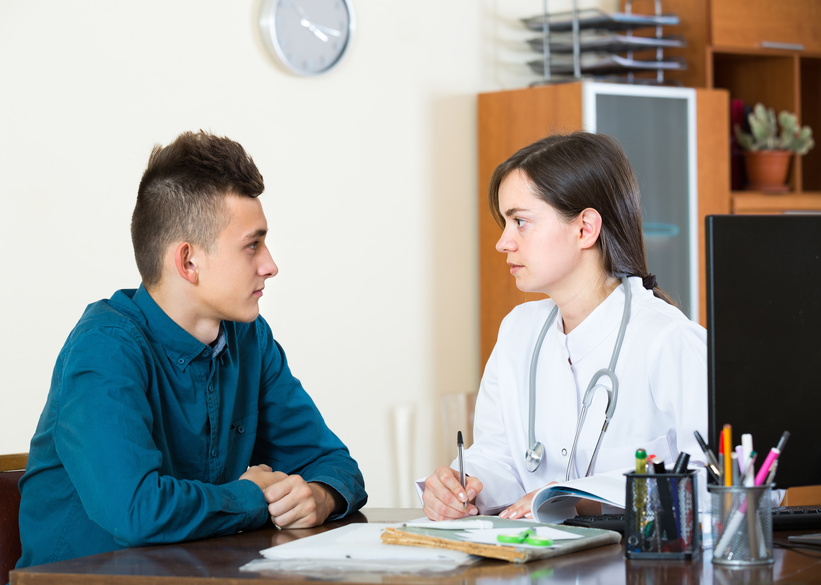 Male teenager and therapeutist at desk in modern clinic